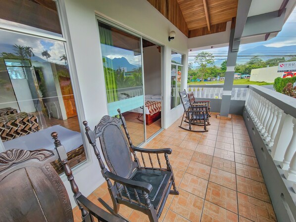 Un balcon doté d’un sol carrelé, d’un fauteuil à bascule en bois, d’un banc rembourré et offrant une vue sur un paysage montagneux.