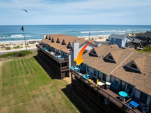 Un bâtiment situé sur la côte, doté de plusieurs terrasses et d’un espace extérieur aménagé, offrant une vue sur la plage et l’océan.
