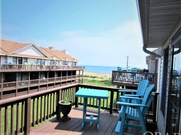 A balcony with a table and chairs, overlooking a beach and buildings.