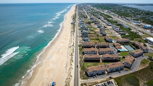 An aerial view of a coastal residential area with a beach, houses, and a road.