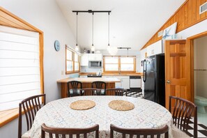A kitchen with a dining table, chairs, a refrigerator, and a window.
