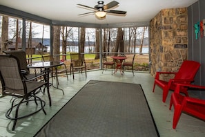 Relax in a serene outdoor space with a view of the water and surrounding trees, featuring a ceiling fan, table, and comfortable seating.