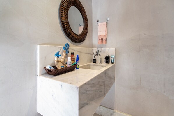 A bathroom with a marble sink, a wooden-framed mirror, and a towel rack with a pink towel.