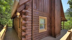 Una cabaña de troncos con una terraza de madera y una ventana con persianas.