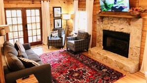 Una sala de estar acogedora con chimenea de piedra, paredes de madera, un televisor grande y una alfombra roja estampada.