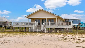 Een huis aan het strand met een houten terras en een trap naar de hoofdingang.