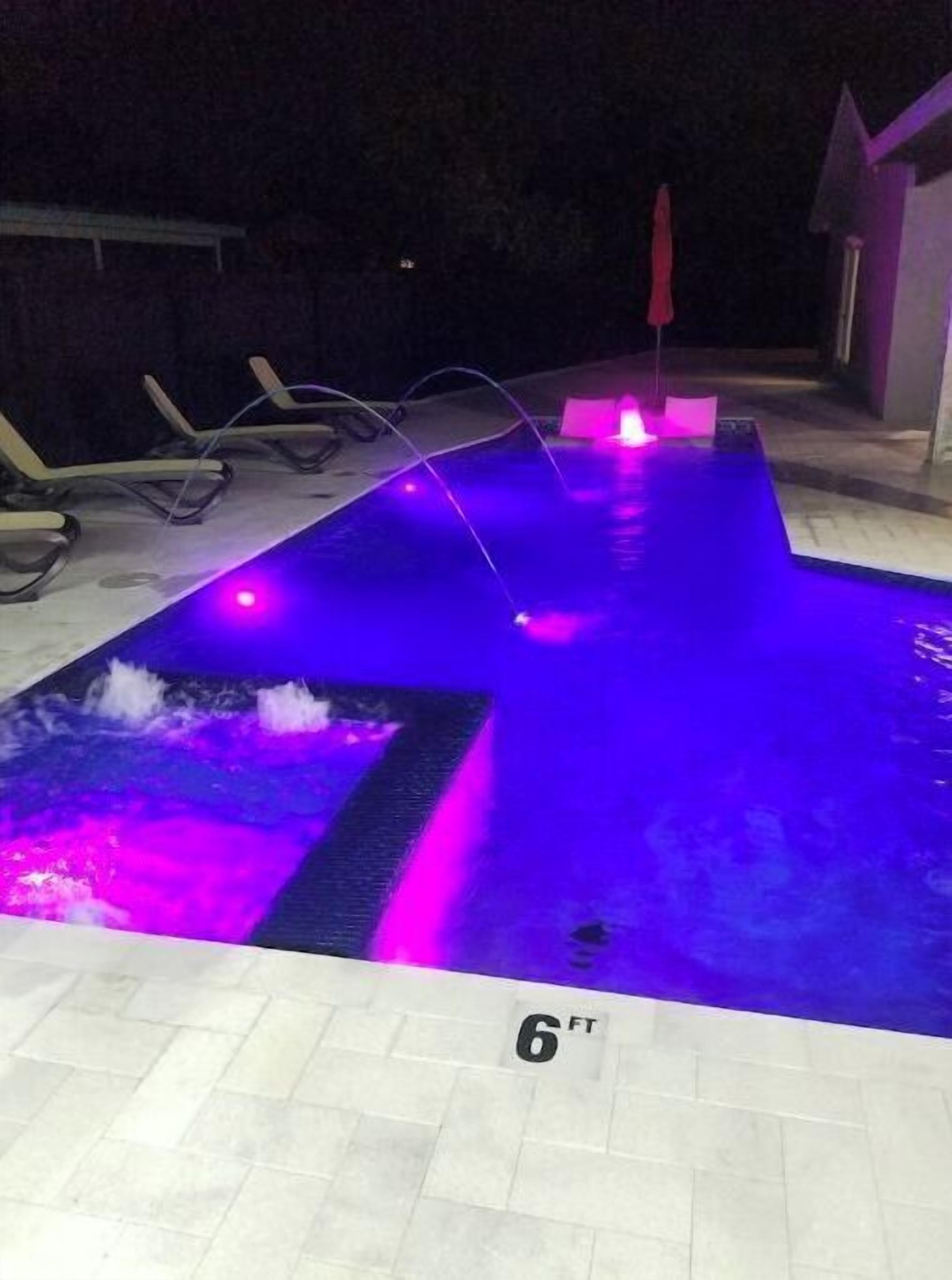A swimming pool with a 6 ft depth marker, surrounded by lounge chairs and a red umbrella.