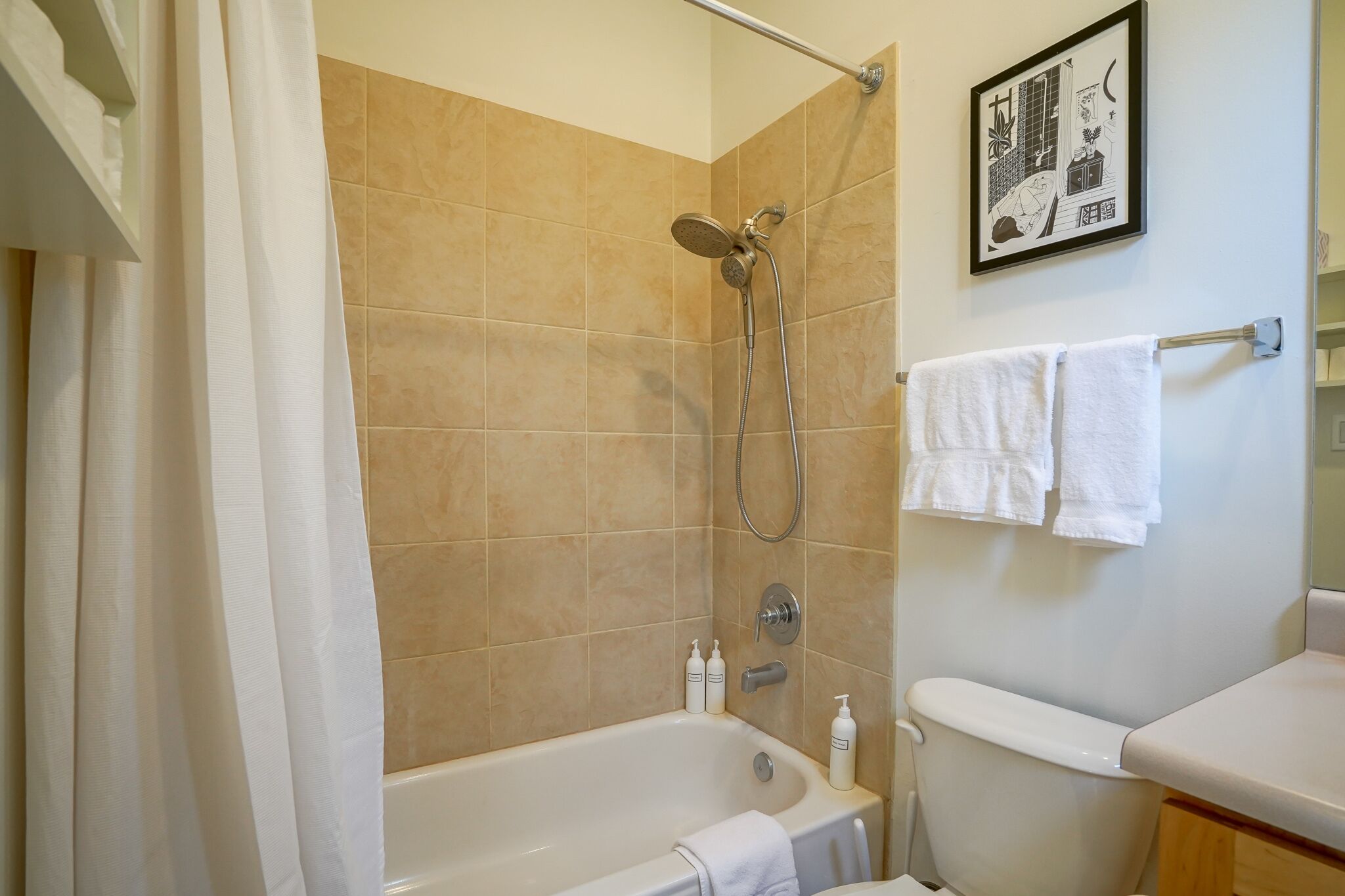 A bathroom with a bathtub, shower, and toilet. There are two white towels hanging on a rack.