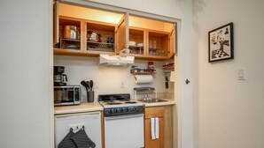Une cuisine compacte équipée d’un four à micro-ondes, d’une cuisinière et d’un four, de placards en bois et d’un petit plan de travail.