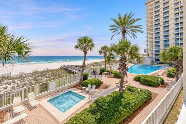 A resort with a pool, lounge chairs, palm trees, and a beach view.