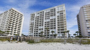 Ein Strandhotel mit mehreren Etagen, Balkonen und einem Sandstrand.