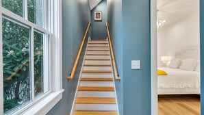 Un escalier en bois, avec des marches et des rampes, menant à une chambre à coucher équipée d’un lit et d’une table de chevet.