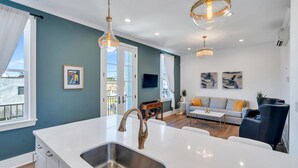 Une cuisine moderne dotée d’un grand îlot central, d’un évier en acier inoxydable et de luminaires suspendus.