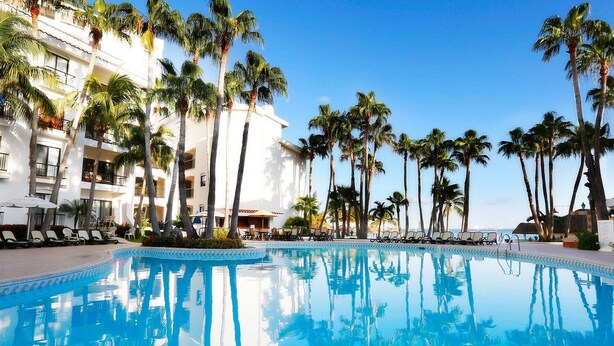 A pool area with palm trees, lounge chairs, and a building with balconies. - 2 Bedroom at The Royal Cancun  (Cancún)