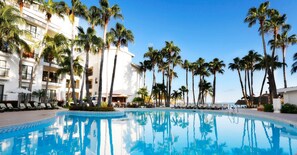 A pool area with palm trees, lounge chairs, and a building with balconies.