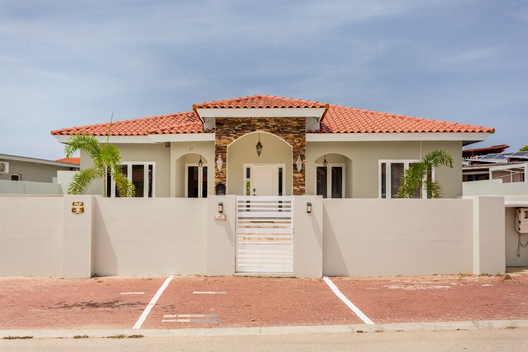 A modern two-story house with a red-tiled roof, a gated entrance, and a paved driveway.