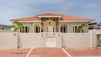 A modern two-story house with a red-tiled roof, a gated entrance, and a paved driveway.