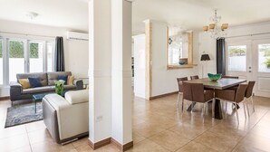 A modern living room with a sofa, coffee table, and a dining area with a table and chairs. - VILLA TOPAZ- 3BR/2BA-5 car min to Palm Beach (Noord)