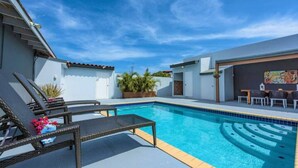 A swimming pool with lounge chairs and a table, surrounded by a white building with a tiled roof. - VILLA TOPAZ- 3BR/2BA-5 car min to Palm Beach (Noord)