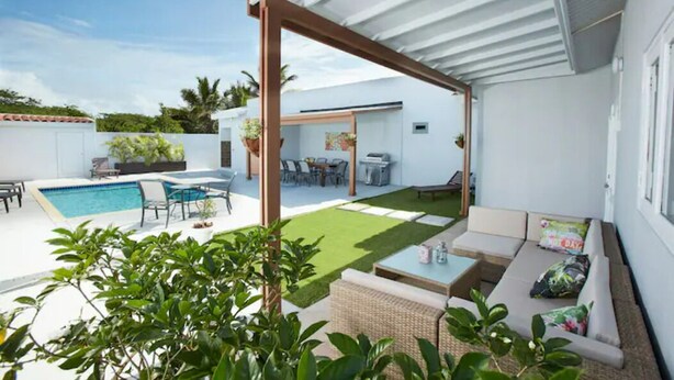A modern outdoor patio with a pool, seating area, and a covered section. - VILLA TOPAZ- 3BR/2BA-5 car min to Palm Beach (Noord)