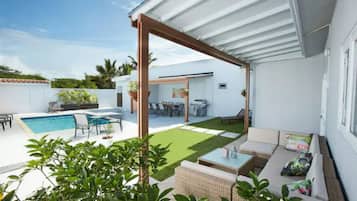 A modern outdoor patio with a pool, seating area, and a covered section.