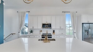 Een moderne keuken met witte kasten, een groot eiland, roestvrijstalen apparatuur en uitzicht op de omgeving.