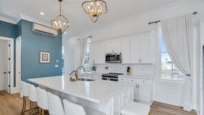 Een moderne keuken met witte kastjes, een centraal eiland met barkrukken, roestvrijstalen apparatuur en uitzicht door het raam.
