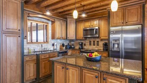 A spacious kitchen with wooden cabinets, a granite countertop, stainless steel appliances, and pendant lighting. - Killen Time on Lake Martin (Dadeville)