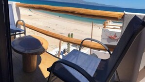 A balcony with a view of a beach and mountains. There is a wooden table and a blue chair. - Beach Front Lofts 4 (el sargento)