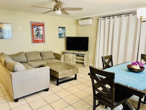 A living room with a sofa, coffee table, TV stand, and dining table with chairs.
