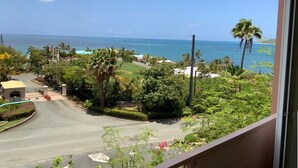 A view from a balcony overlooking a coastal area with a road, greenery, and a clear blue sky. - Caribbean Dream - located in the community of Coakley Bay! (Christiansted)