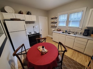 A compact kitchen with a refrigerator, stove, and sink. There is a dining table with chairs and a red tablecloth.
