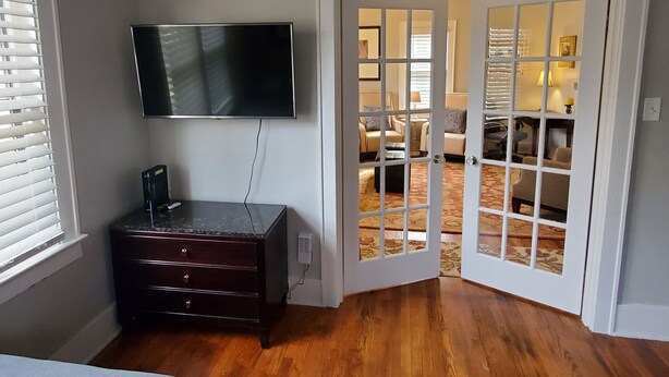 A room with a flat-screen TV mounted on the wall, a dark wooden dresser, and a door leading to a living area with a patterned carpet. - Southern Charm: Home is minutes from downtown w/a cozy sitting porch (Nashville)
