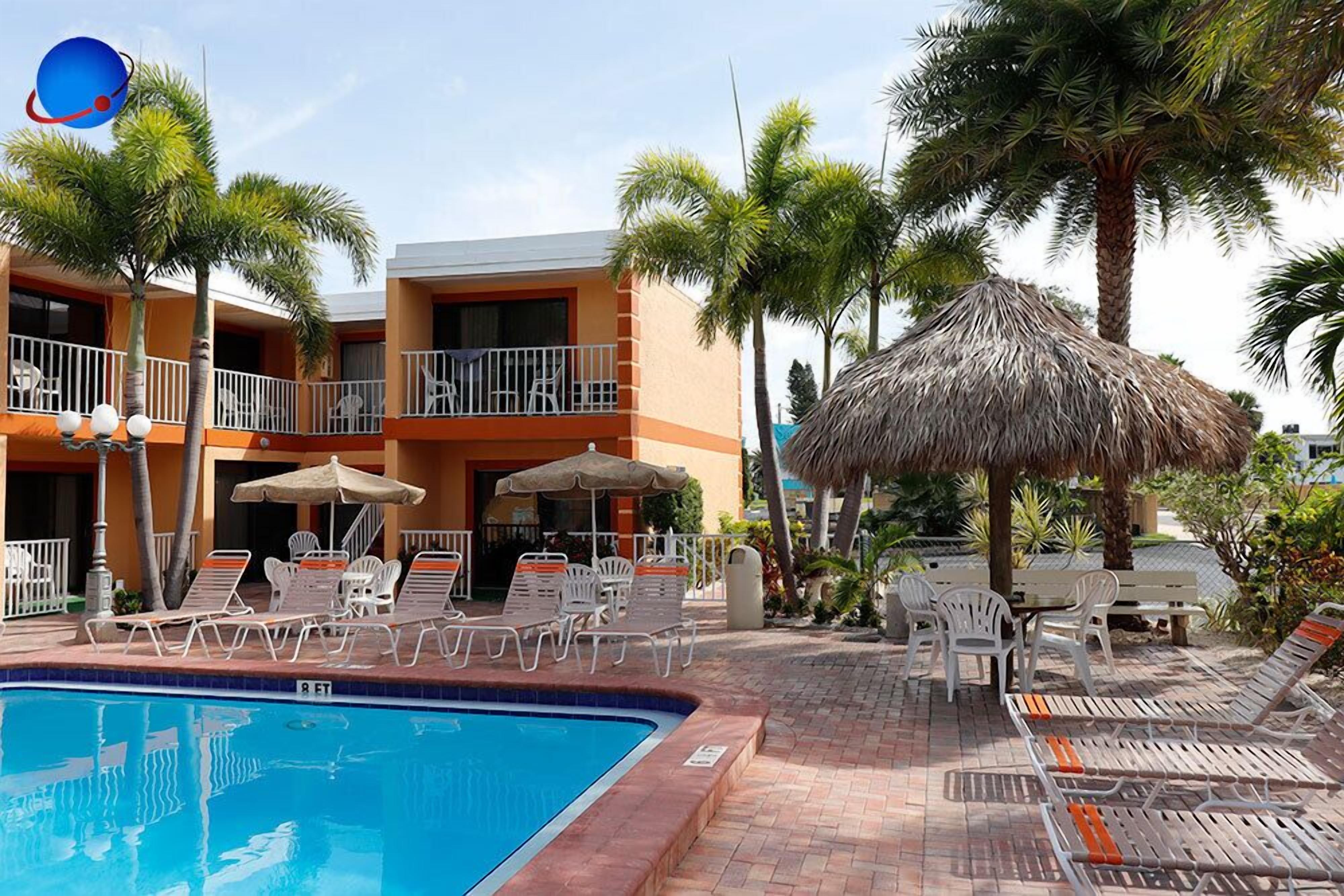 Un hotel con piscina, sillas de descanso, sombrillas y palmeras.