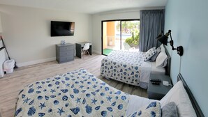 A hotel room with two beds, a desk, a chair, a TV, and a balcony with a view of a pool. - Satellite Motel - Seaclusion 104 (Treasure Island)