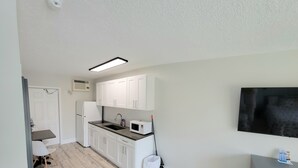A modern kitchen with white cabinets, a microwave, and a sink. There is a dining area with a table and chairs, and a gray dresser with drawers. - Satellite Motel - Seaclusion 104 (Treasure Island)