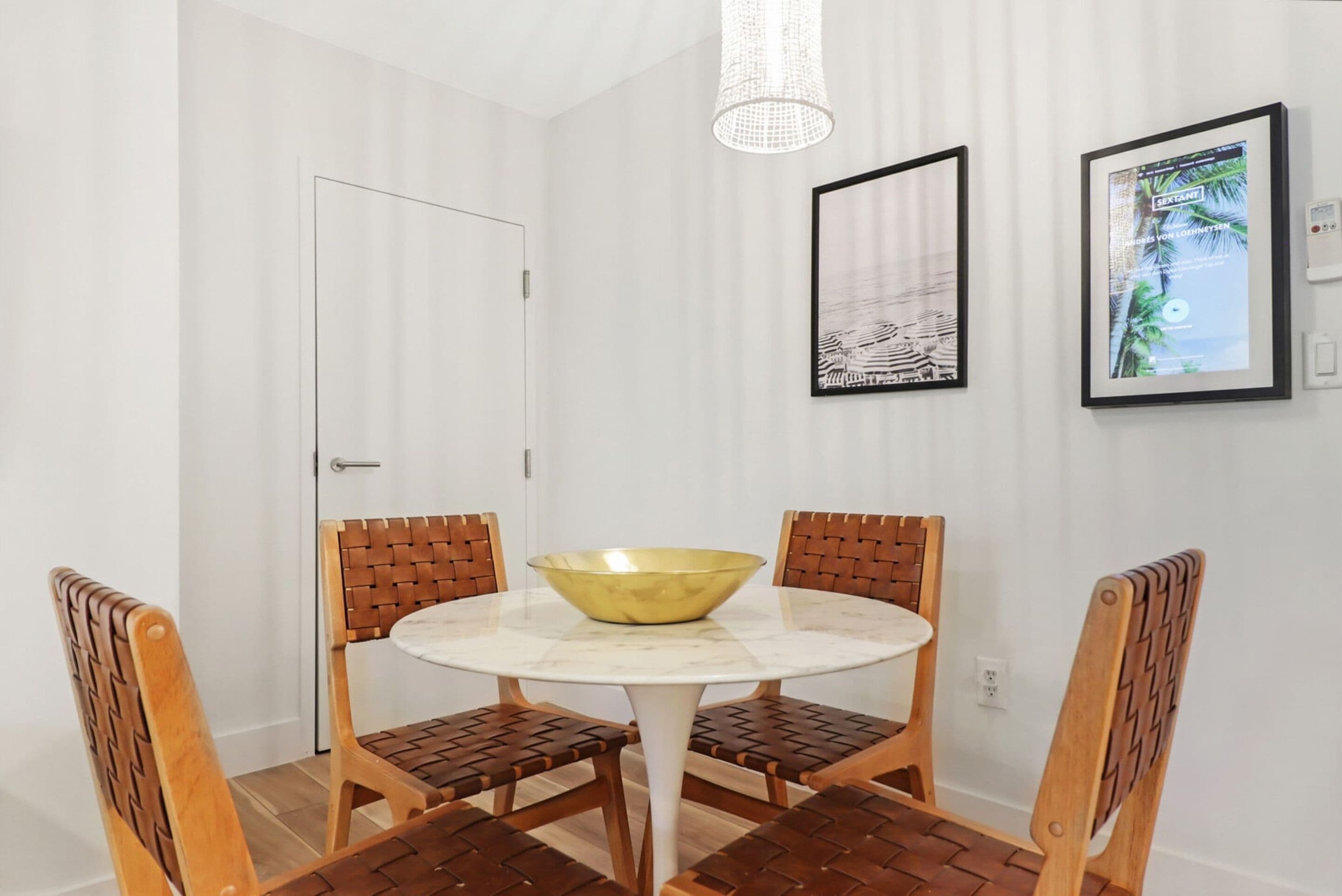Un comedor con una mesa redonda, cuatro sillas de madera, un cuenco dorado y cuadros en las paredes.