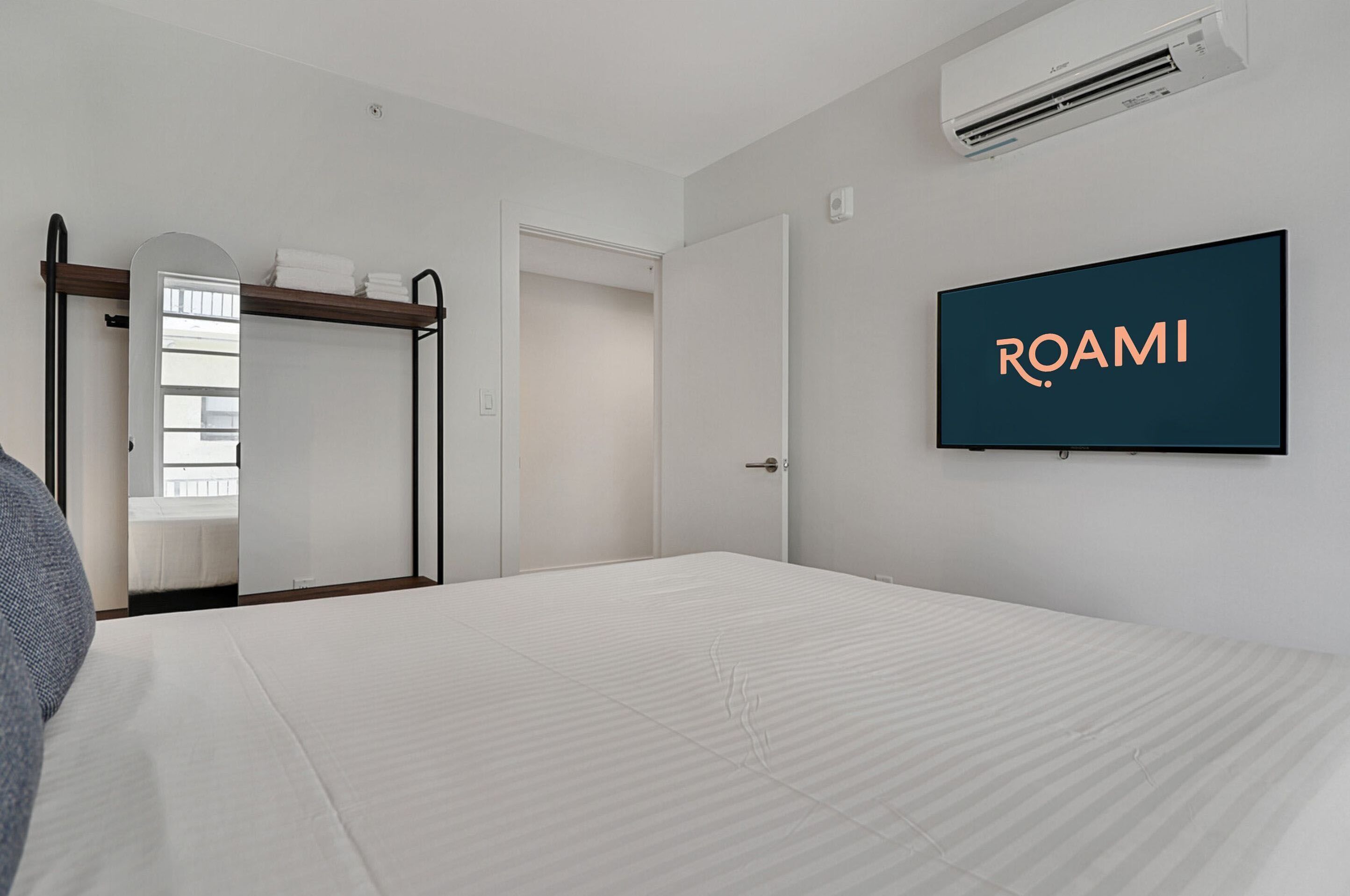 Een moderne hotelkamer met een bed, een kledingkast, een spiegel en een televisie waarop 