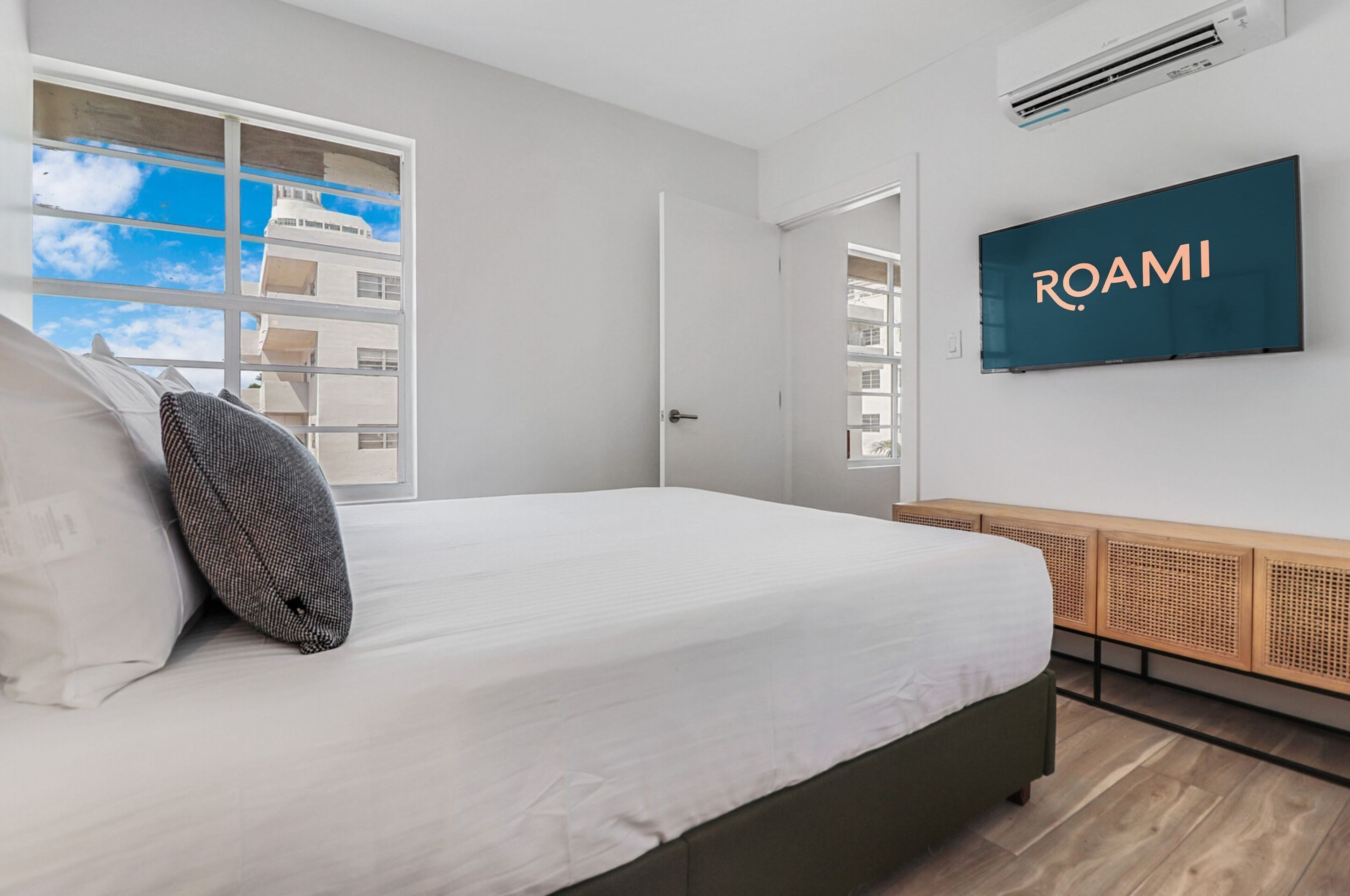 A modern hotel room with a large bed, a TV mounted on the wall, and a window with a view of buildings.