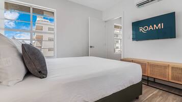 A modern hotel room with a large bed, a TV mounted on the wall, and a window with a view of buildings.