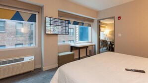 A hotel room with a bed, a desk, and a window overlooking a brick building.