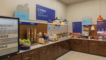 Zona de desayuno tipo buffet con secciones identificadas para yogur, huevos, leche y comida caliente.