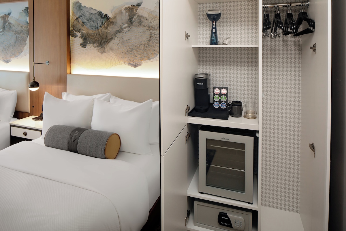 Habitación de hotel con cama, cafetera, microondas y zapatero.