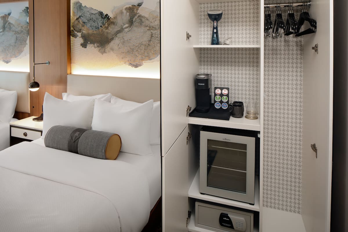 A hotel room with a bed, a coffee maker, a microwave, and a shoe rack.