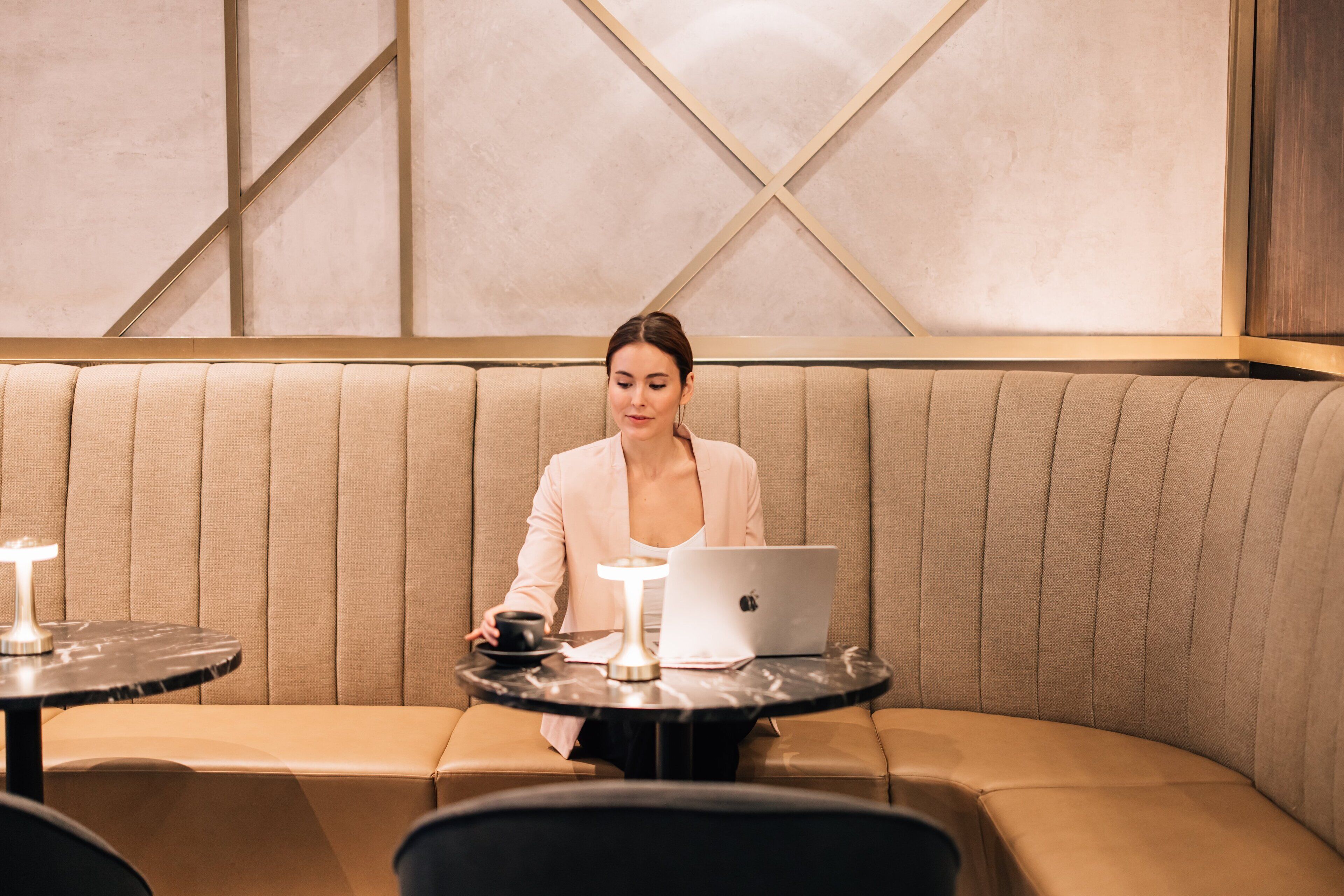 Une personne est assise sur un canapé beige, un ordinateur portable et une tasse sont à portée de main, dans une pièce dont le mur est décoré de motifs géométriques.
