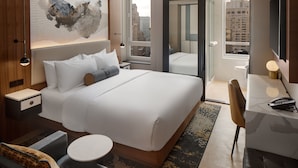 Una habitación de hotel moderna con una cama grande, un escritorio, una silla y vistas a la ciudad a través de la ventana.