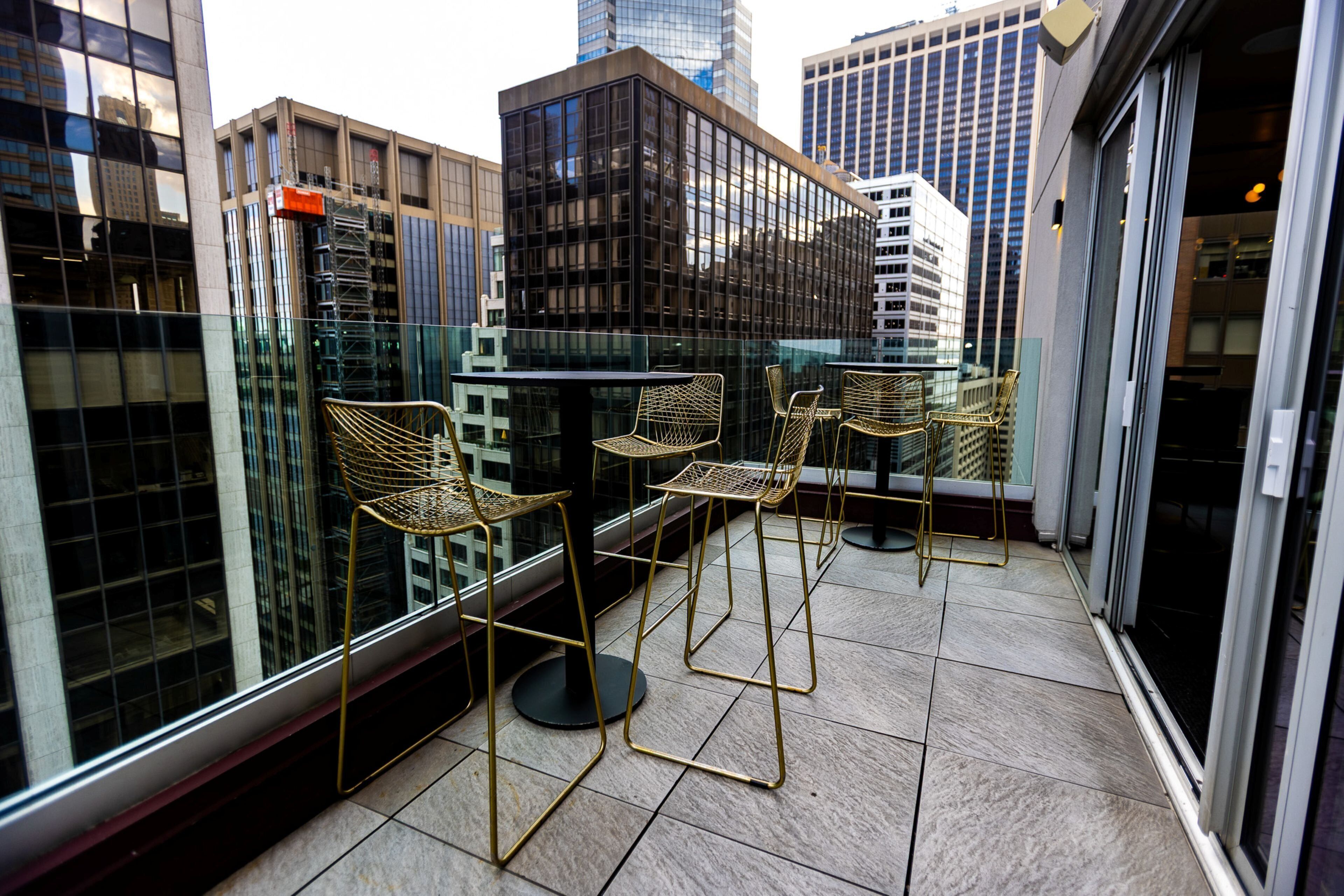 A balcony with four wicker chairs and a small table, overlooking a cityscape with tall buildings.