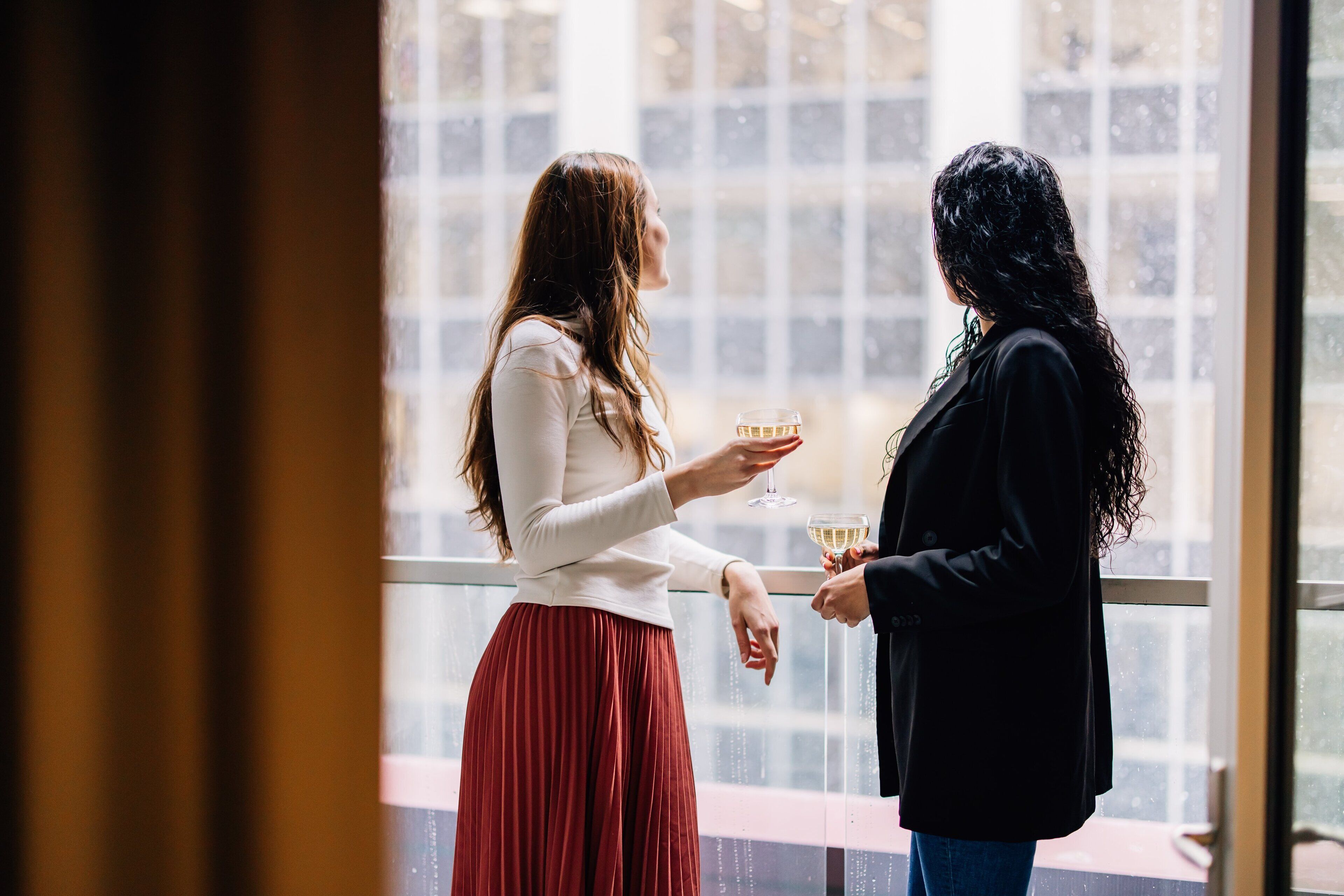 Dos personas de pie junto a una ventana con vistas a edificios.