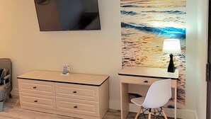 Un dormitorio con cama, escritorio, silla, televisor montado en la pared y un amplio mural de playa.