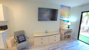 Un dormitorio con cama, escritorio, silla, cómoda y televisor de pared.